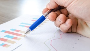 Ausgedrucktes Bild mit Diagrammen sowie eine Hand, die einen Kugelschreiber hält