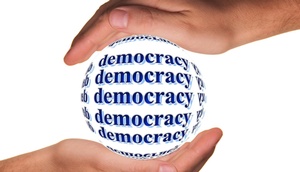 Eine Kugel mit Schriftzug Democracy in Händen gehalten.