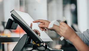 Hand tippt etwas auf Kassensystem ein und hält Rechnung