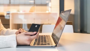 Person sitzt mit Kreditkarte vor einem Laptop