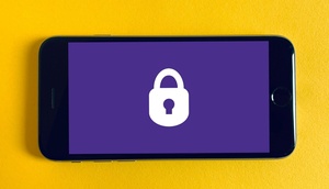 Mobiltelefon mit lila Display mit großem weißen Vorhängeschloss, gelber Hintergrund 