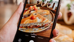 Hand hält Handy auf dem ein Foto mit Essen abgebildet ist
