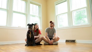 Junge Frau, junger Mann, Hund sitzen am Boden einer hellen, leeren Wohnung 