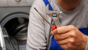 Handwerker mit Werkzeug in der Hand, im Hintergrund Waschmaschine