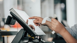 Hand tippt etwas auf Kassensystem ein und hält Rechnung