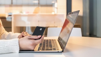 Person sitzt mit Kreditkarte vor einem Laptop