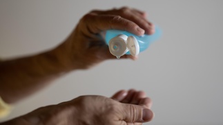 Hände eines älteren Menschen, Desinfektionsmittel  in blauer Plastikflasche