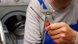 Handwerker mit Werkzeug in der Hand, im Hintergrund Waschmaschine