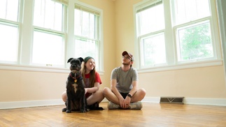 Junge Frau, junger Mann, Hund sitzen am Boden einer hellen, leeren Wohnung 