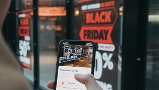 Männerhand hält Smartphone vor einem Schaufenster, das 50%-Rabatt am Black Friday bewirbt.