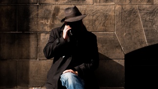 Mann mit Hut sitzt auf einer Bank und telefoniert mit dem Handy
